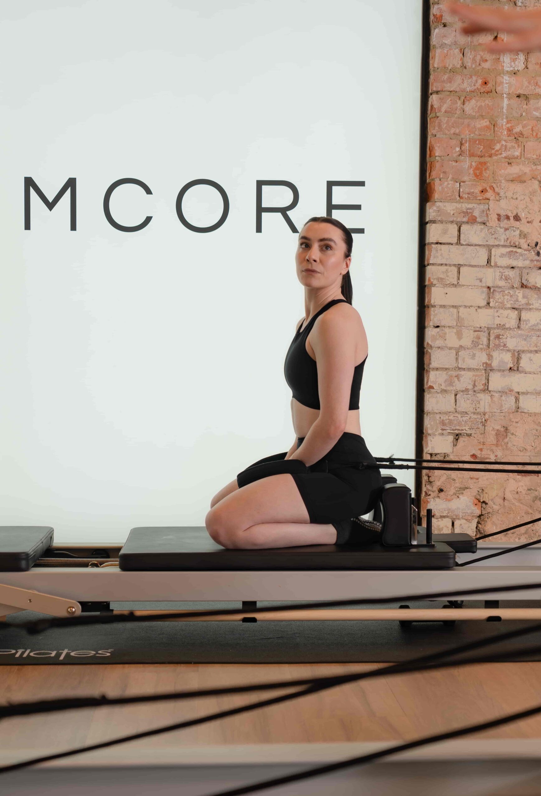 Client seated in an upright position on the Reformer carriage at Reformcore, preparing for a strength-focused Pilates sequence in a minimalist, design-led studio space.