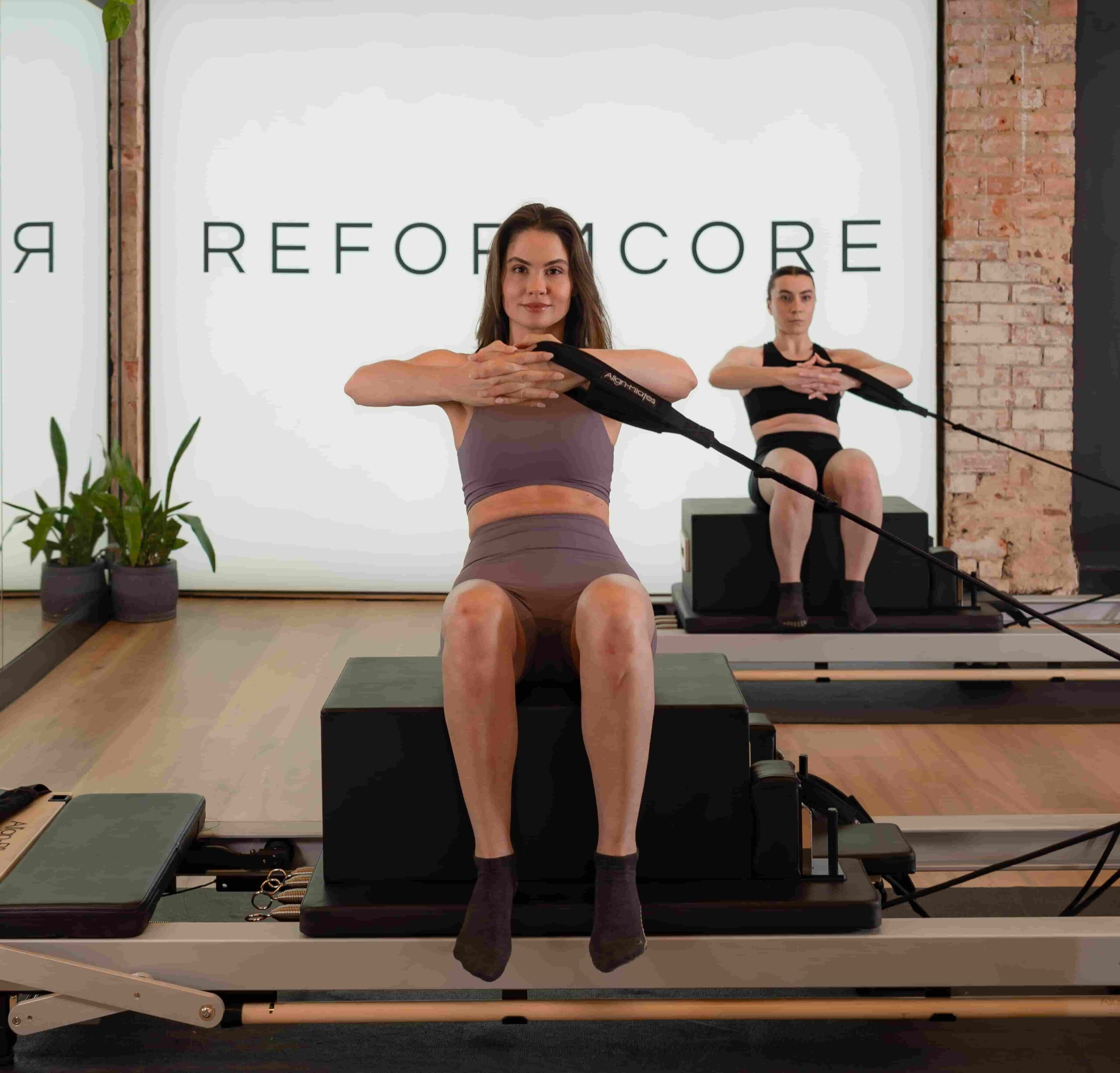 Clients seated on Reformers at Reformcore, performing resistance band core rotations to build stability, strength, and precision in a high-end Pilates studio.