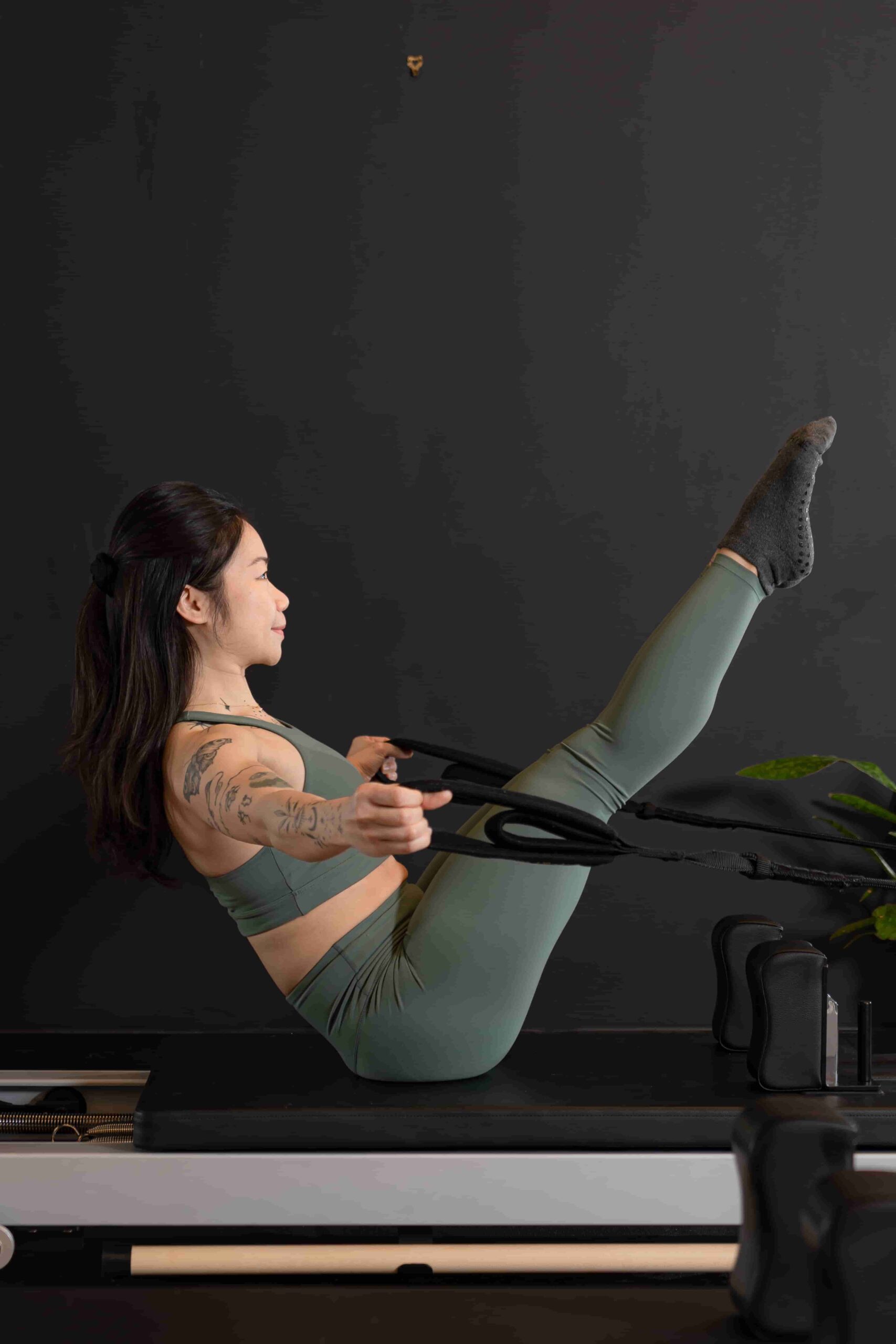 Reformcore instructor demonstrating advanced core control in a V-sit position on the Reformer, using resistance straps to enhance strength, balance, and flexibility.