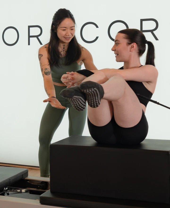 Reformcore instructor guiding a client through a resistance-based oblique twist on the Reformer, targeting core strength and stability in a premium Pilates setting.