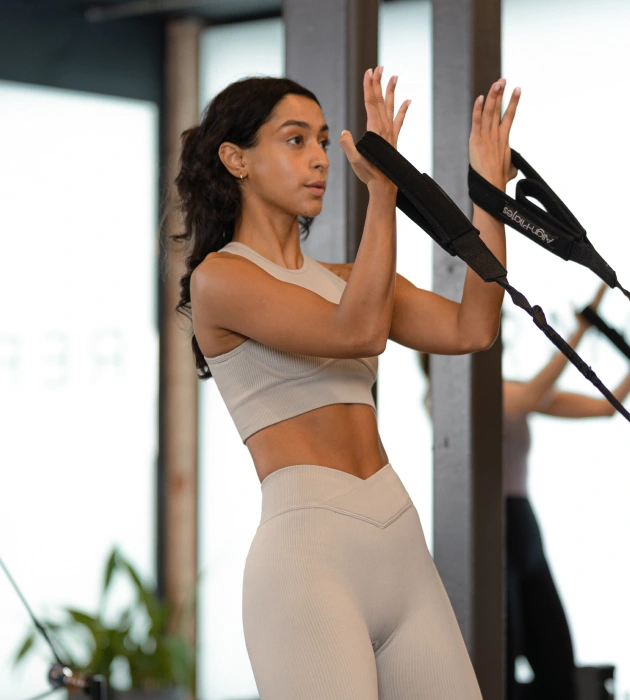 Client performing a standing resistance movement on the Reformer at Reformcore, activating arms and core for full-body control and strength in a contemporary Pilates studio.