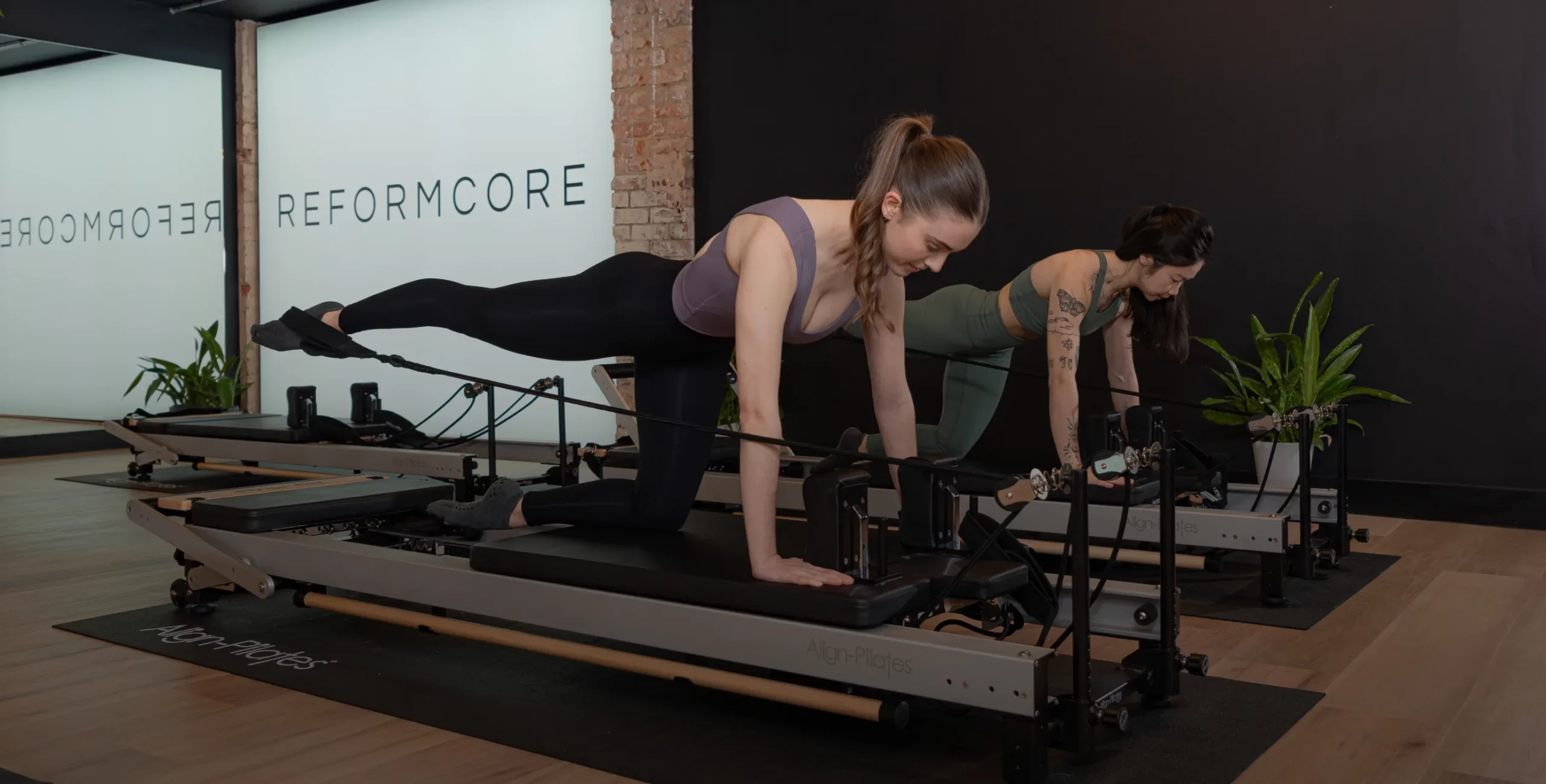 Reformcore clients in a Pilates class performing glute kickbacks on the Reformer, targeting lower body strength, balance, and core stability in a boutique studio setting.
