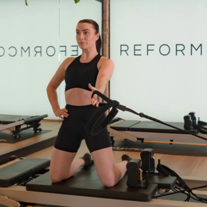 Client performing kneeling arm work with resistance straps on the Reformer at Reformcore, targeting posture, shoulder strength, and full-body alignment in a modern Pilates studio.