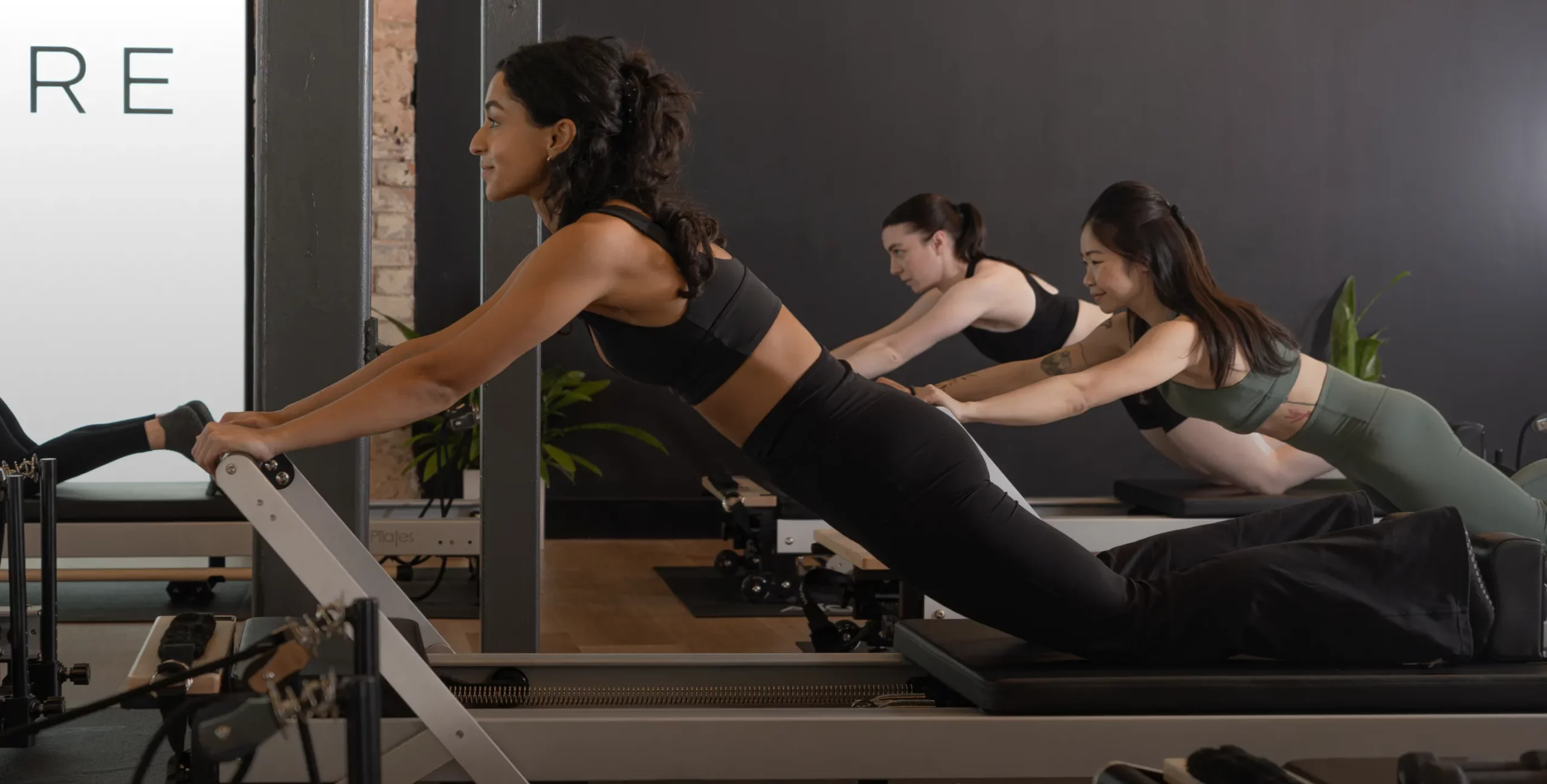 "Reformcore clients in a Pilates class performing a kneeling lat pull on the Reformer, enhancing upper body control, core activation, and full-body stability in a premium studio environment.